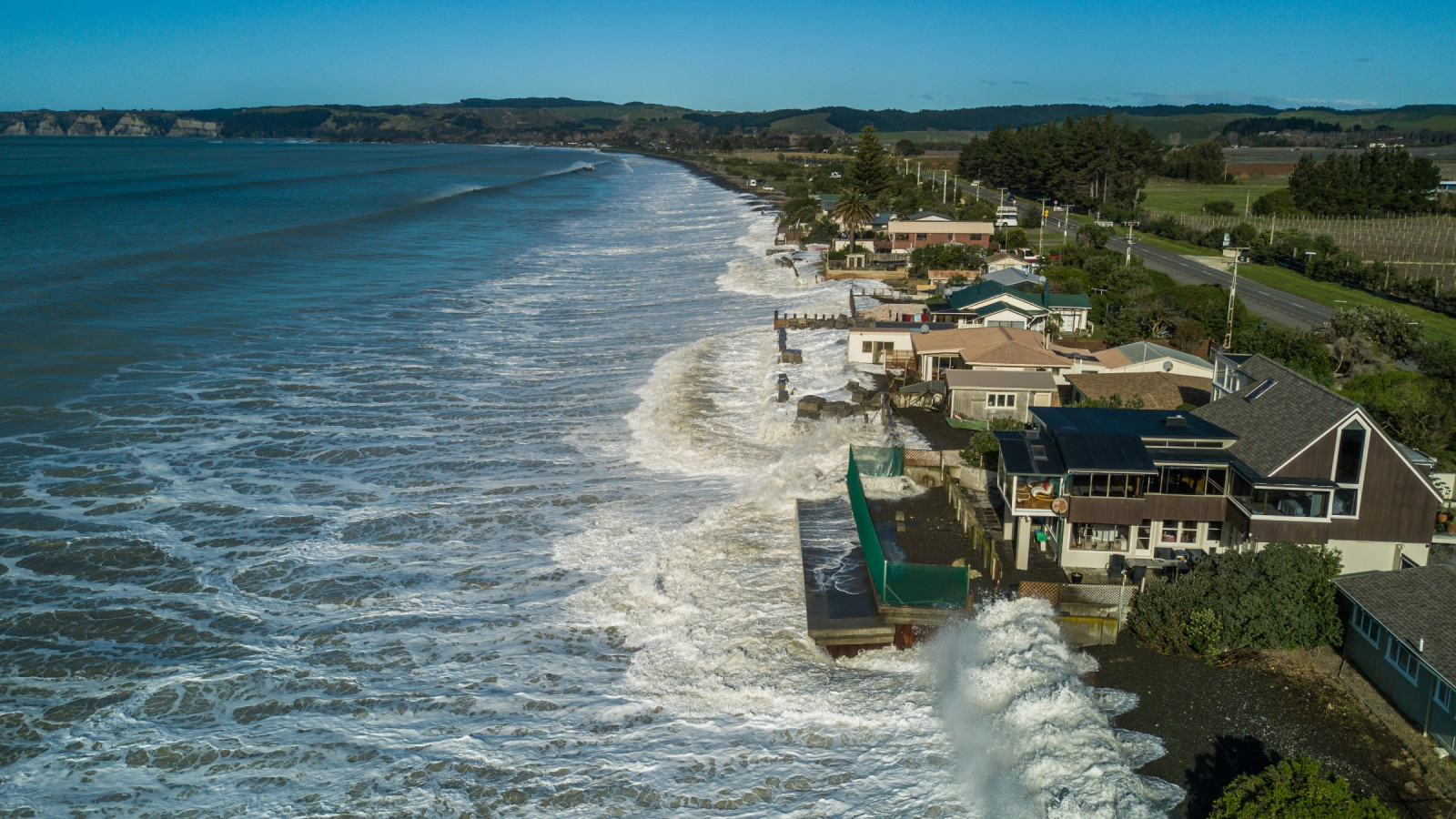 A coastline with a line of houses being breached and flooded by the ocean.